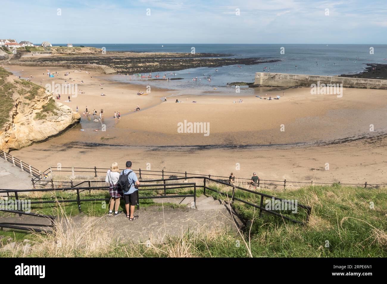 Couple looking out over Cullercoats Bay with holidaymakers on the beach and in the sea, England, UK Stock Photo