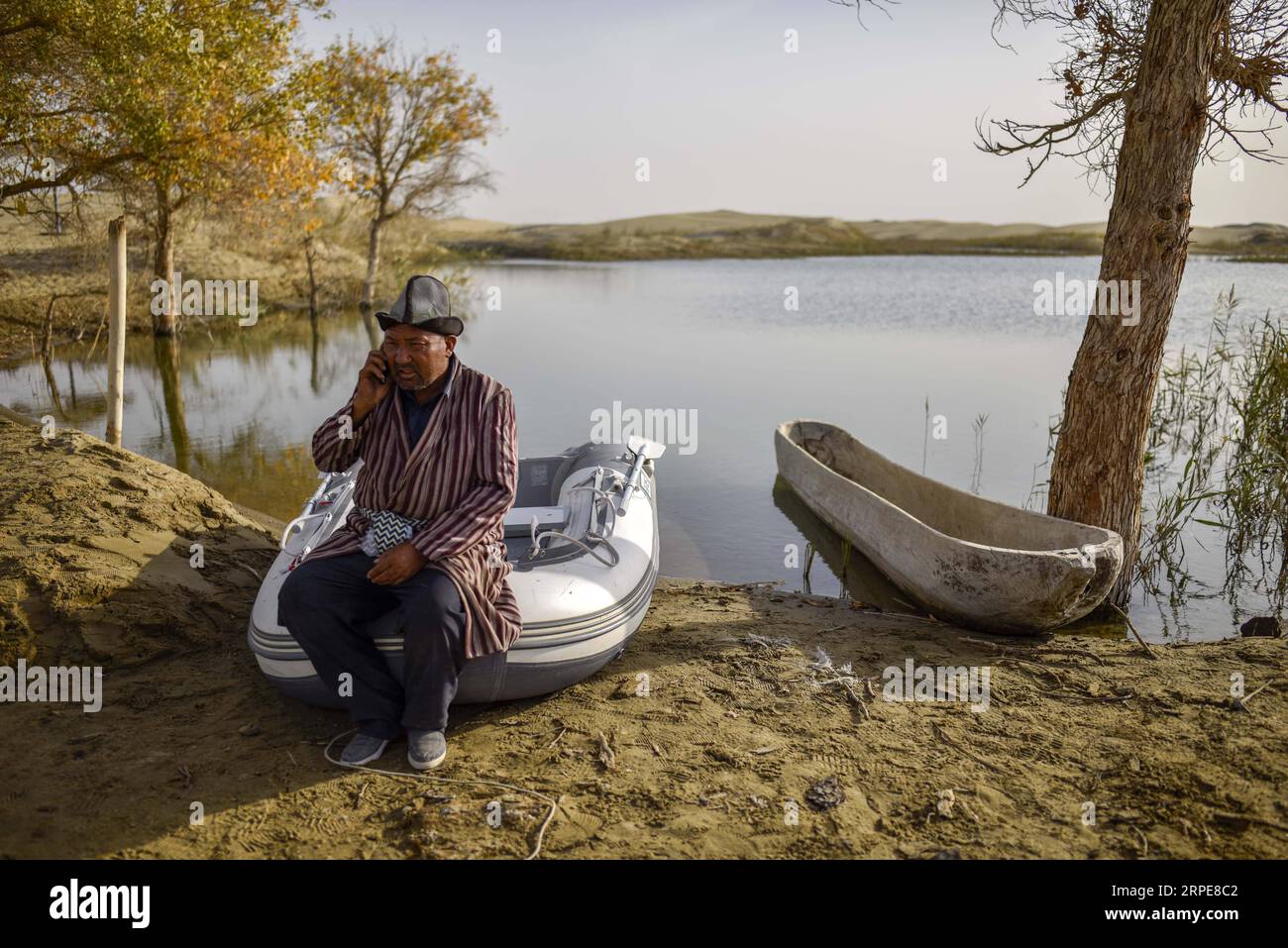 (190821) -- YULI, Aug. 21, 2019 -- Amudun Abudu answers his cellphone in Lop Nur People Village in Yuli County, northwest China s Xinjiang Uygur Autonomous Region, Oct. 16, 2018. Lop Nur People Village is located in Yuli County, where Tarim River flows through the deserts with populus euphratica forests reflection on the shimmering waves. Amudun Abudu, a 61-year old typical Lop Nur villager, works in local tourism industry. With the changes of the times, many Lop Nur people have various options for a living, yet he insists on the tradition of fishing in rivers and lakes. Not only does he make Stock Photo