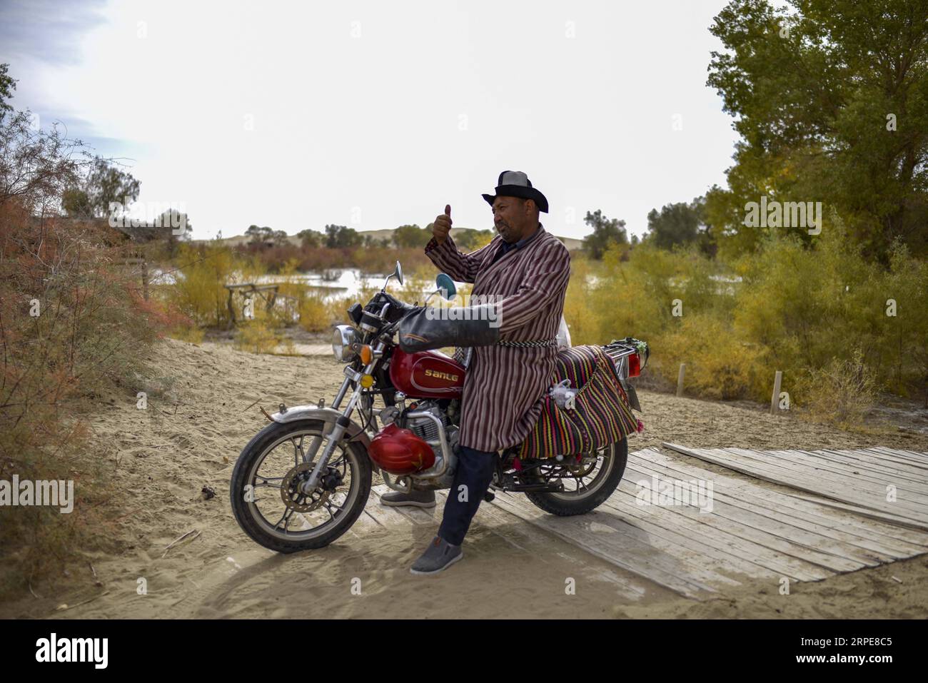 (190821) -- YULI, Aug. 21, 2019 -- Amudun Abudu greets visitors in Lop Nur People Village in Yuli County, northwest China s Xinjiang Uygur Autonomous Region, Oct. 16, 2018. Lop Nur People Village is located in Yuli County, where Tarim River flows through the deserts with populus euphratica forests reflection on the shimmering waves. Amudun Abudu, a 61-year old typical Lop Nur villager, works in local tourism industry. With the changes of the times, many Lop Nur people have various options for a living, yet he insists on the tradition of fishing in rivers and lakes. Not only does he make delici Stock Photo