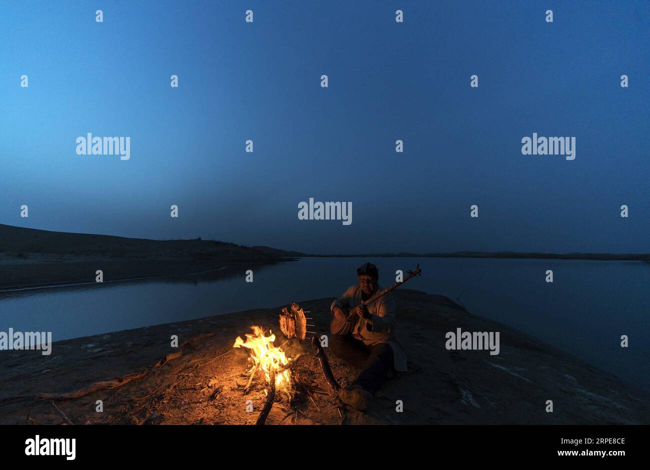 (190821) -- YULI, Aug. 21, 2019 -- Amudun Abudu plays an instrument in Lop Nur People Village in Yuli County, northwest China s Xinjiang Uygur Autonomous Region, April 11, 2019. Lop Nur People Village is located in Yuli County, where Tarim River flows through the deserts with populus euphratica forests reflection on the shimmering waves. Amudun Abudu, a 61-year old typical Lop Nur villager, works in local tourism industry. With the changes of the times, many Lop Nur people have various options for a living, yet he insists on the tradition of fishing in rivers and lakes. Not only does he make d Stock Photo