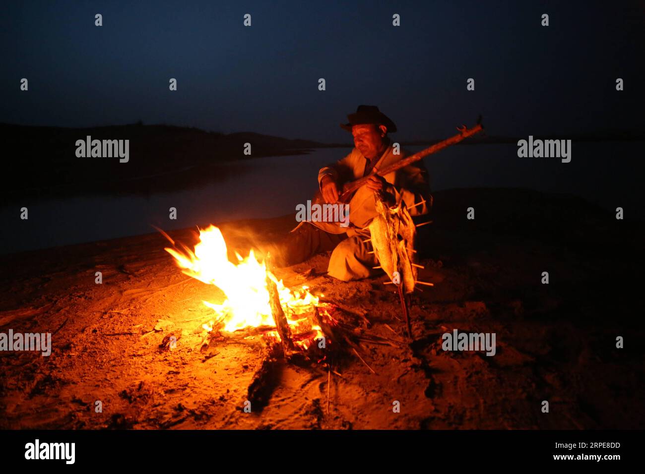 (190821) -- YULI, Aug. 21, 2019 -- Amudun Abudu plays an instrument in Lop Nur People Village in Yuli County, northwest China s Xinjiang Uygur Autonomous Region, April 11, 2019. Lop Nur People Village is located in Yuli County, where Tarim River flows through the deserts with populus euphratica forests reflection on the shimmering waves. Amudun Abudu, a 61-year old typical Lop Nur villager, works in local tourism industry. With the changes of the times, many Lop Nur people have various options for a living, yet he insists on the tradition of fishing in rivers and lakes. Not only does he make d Stock Photo