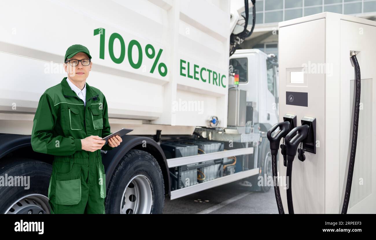 Manager with a digital tablet next to electric garbage truck and ekectric vehicles charging station. Stock Photo