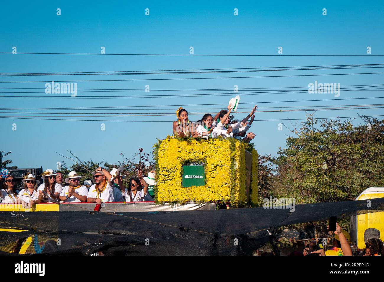 Barranquilla, Atlantico, Colombia - February 18 2023: Men and Women  Dressed in White on a Yellow Box on a Float in the Carnival Parade Wave to a Crow Stock Photo