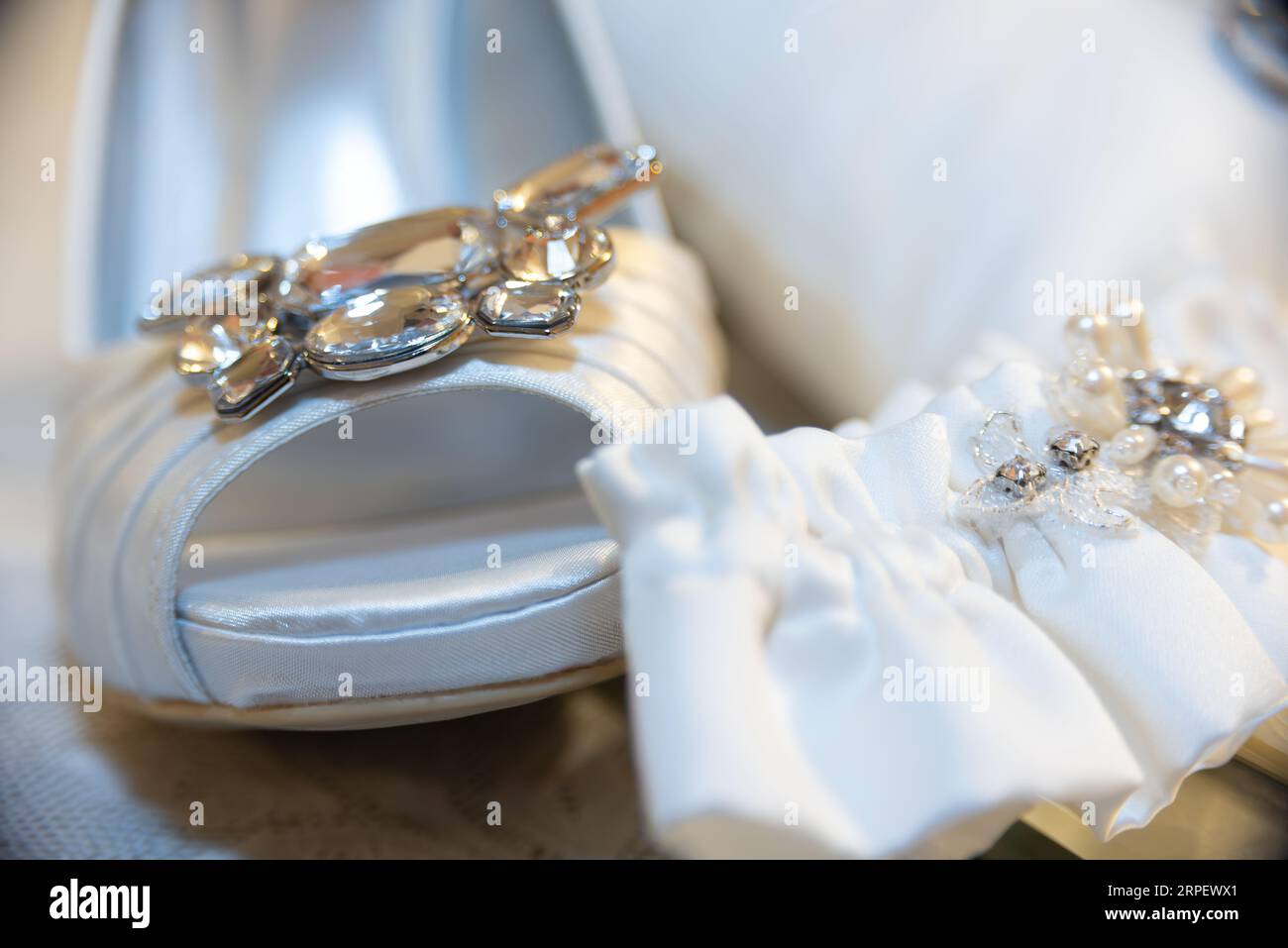 A pair of white satin shoes decorated with two ornate beaded wedding garters Stock Photo