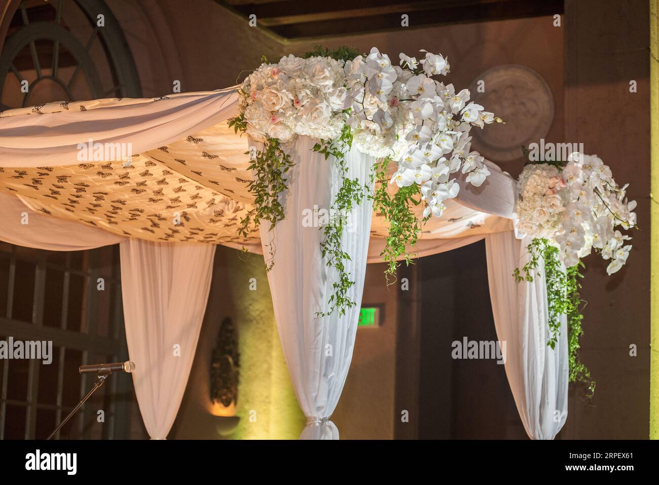 An outdoor wedding venue featuring a floral-covered canopy adorned with curtains and drapes for a romantic and elegant atmosphere Stock Photo