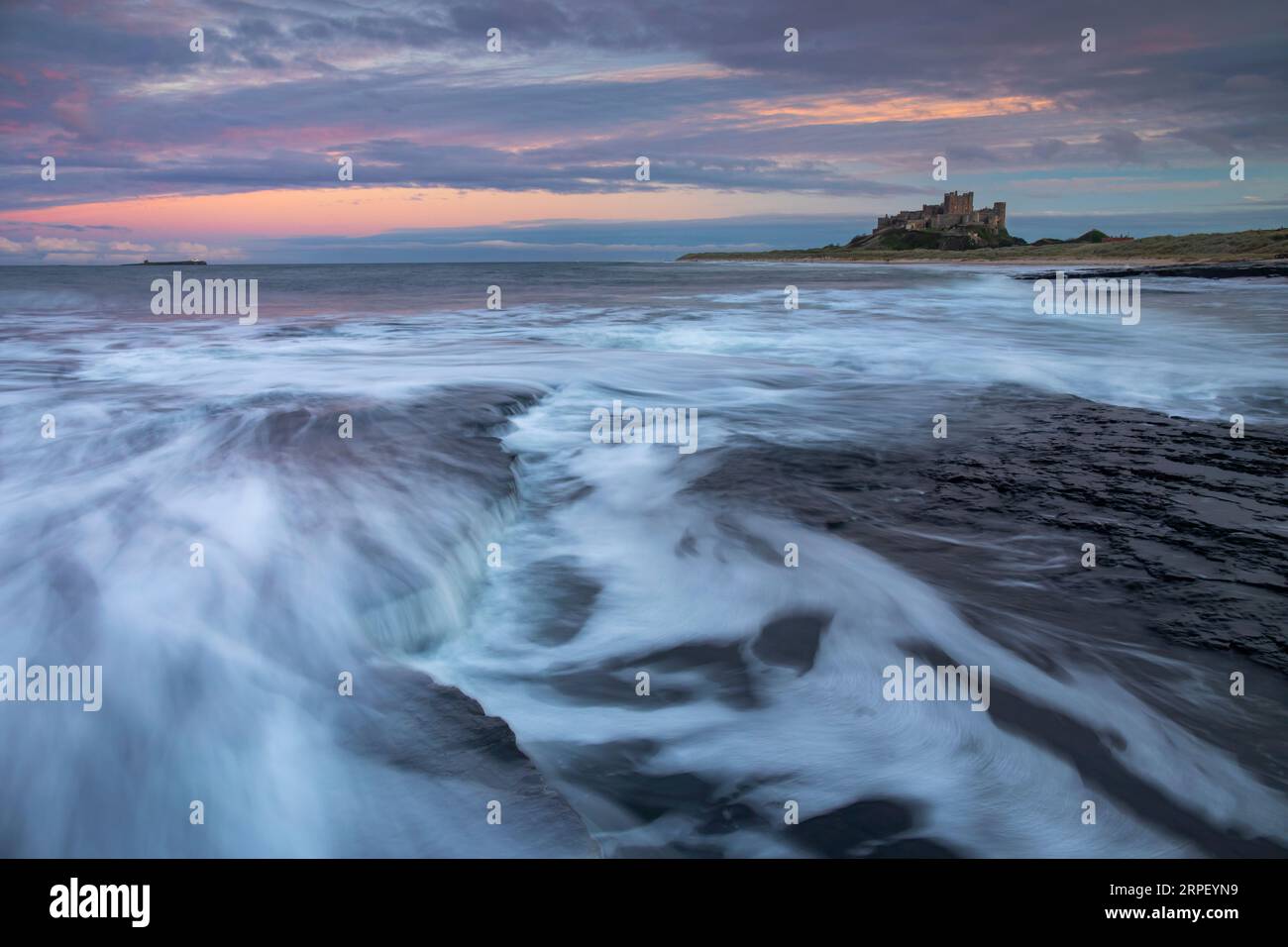Incoming tide and colourful sunset at Bamburgh with Bamburgh Castle in the background (November) Bamburgh, Northumberland, UK Stock Photo