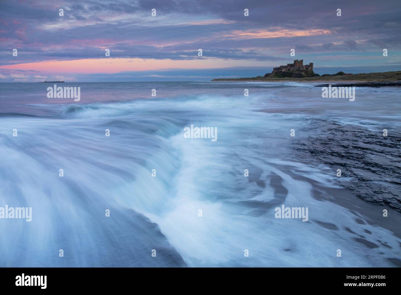 Incoming tide and colourful sunset at Bamburgh with Bamburgh Castle in the background (November) Bamburgh, Northumberland, UK Stock Photo