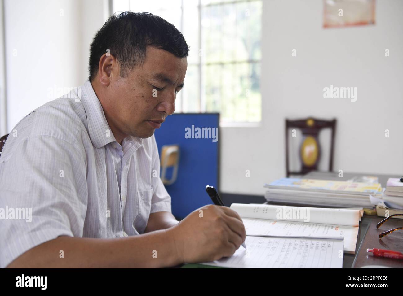 (190908) -- TIANDONG, Sept. 8, 2019 -- Wei Guoji prepares lessons at the office of Tuogua Primary School at Tuogua Village in Zuodeng Yao Ethnic Township of Tiandong County, south China s Guangxi Zhuang Autonomous Region, Sept. 3, 2019. Located in remote mountains of Tiandong county, Tuogua primary school is over 60 km away from the county seat, to which only a rugged mountain road can lead. The 53-year-old Wei Guoji, a native to the village, is the principal of the village school. Wei was recruited as a substitute teacher of the school after graduation from junior high school at the age of 18 Stock Photo