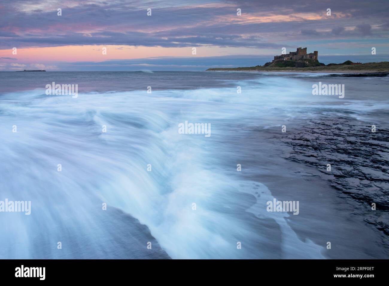 Incoming tide and colourful sunset at Bamburgh with Bamburgh Castle in the background (November) Bamburgh, Northumberland, UK Stock Photo