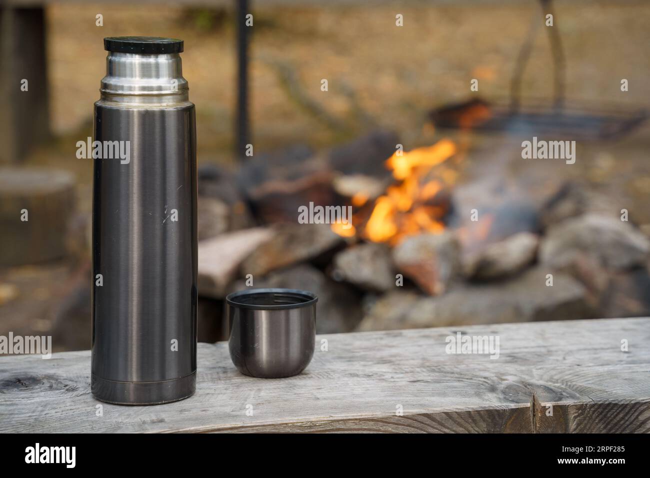 Scratched steel thermos bottle on a wooden bench next to the campfire Stock Photo