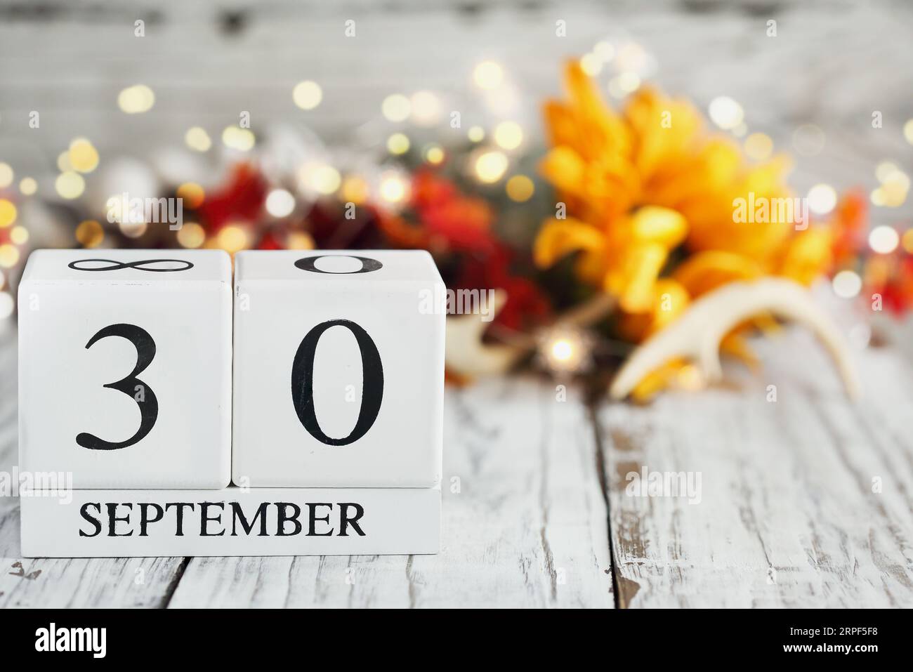 White wood calendar blocks with the date September 30th and autumn decorations over a wooden table. Selective focus with blurred background. Stock Photo