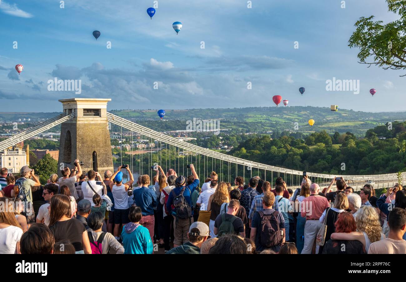 Crowd of spectators watching mass ascent of hot-air balloons at Bristol Balloon Fiesta in sky above Clifton Suspension Bridge Stock Photo