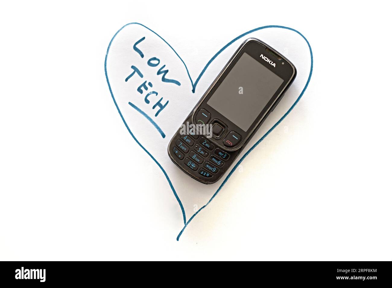 Used cell phone Nokia 6303 ci in a green heart, white background. Concept of loving sustainable, durable, efficient, simple, and maintainable low-tech. Stock Photo