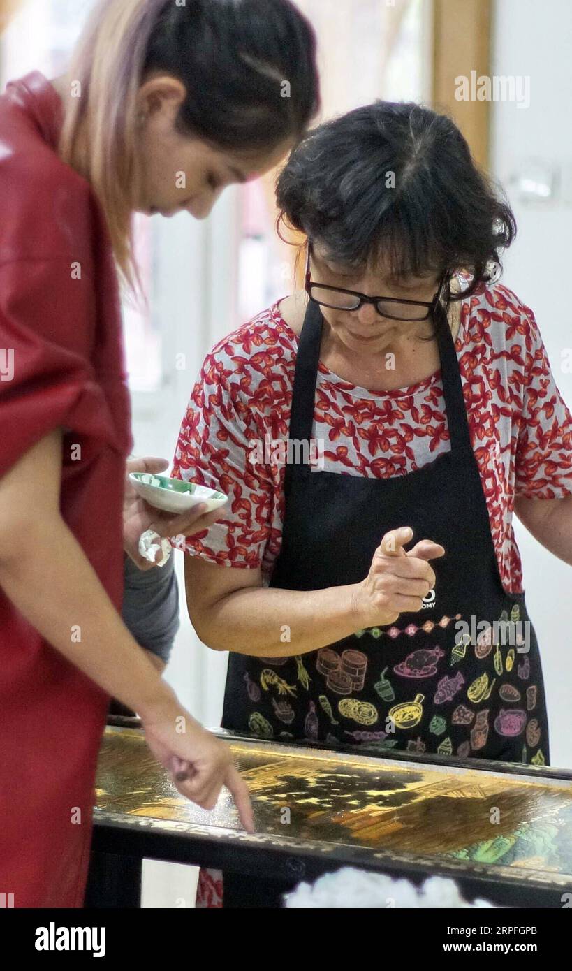 190924 -- BEIJING, Sept. 24, 2019 -- Hu Xin R explains the methods of lacquer painting to a student at Beijing Gold Lacquer Inlaid Co., Ltd. in Beijing, capital of China, Sept. 19, 2019. Gold inlaid lacquer, an integral part of painted and inlaid lacquer, is among the eight Beijing-style handicrafts. Gold inlaid lacquer ware combines the intricate skills of carving, filling, whetting, inlaying and painting. It features a gold lacquered surface inlaid with various gems and other exotic materials. Hu Xin, a 62-year-old senior arts and crafts master of Beijing, has been dedicated to designing and Stock Photo