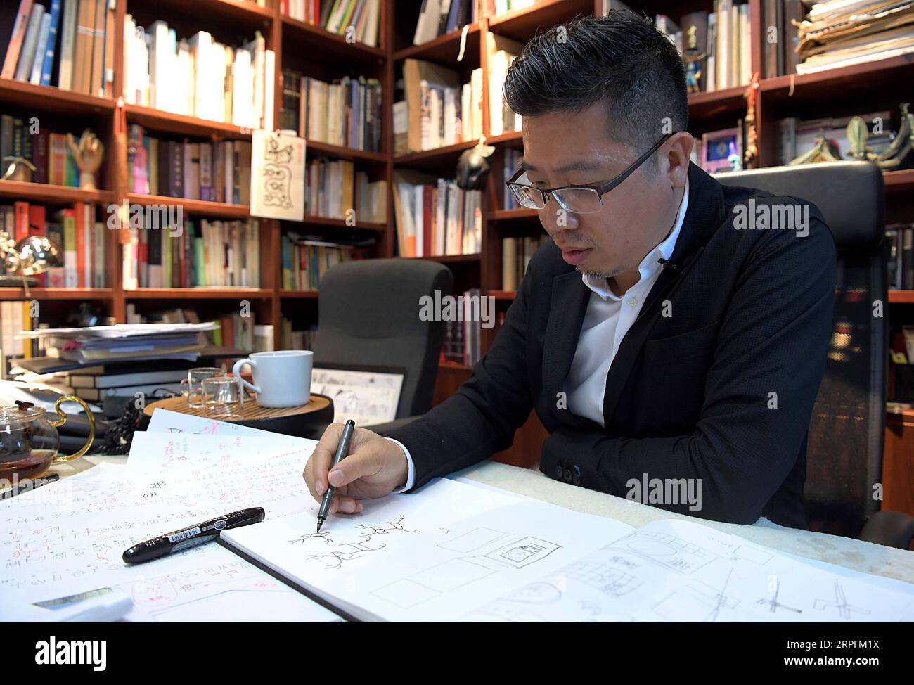 190927 -- BEIJING, Sept. 27, 2019 -- Chen Nan draws a design manuscript at his studio in Tsinghua University in Beijing, capital of China, Sept. 24, 2019. Boasting a history of more than 3,000 years, oracle bone script, the earliest Chinese writing inscriptions carved on tortoise shells and animal scapulas, has been given modern meanings with a new series of emojis, thanks to the efforts made by Chen Nan. Chen, a professor at the Academy of Arts and Design of Tsinghua University, has devoted himself to studying and designing oracle bone script since 1999. So far, Chen has issued six sets of an Stock Photo