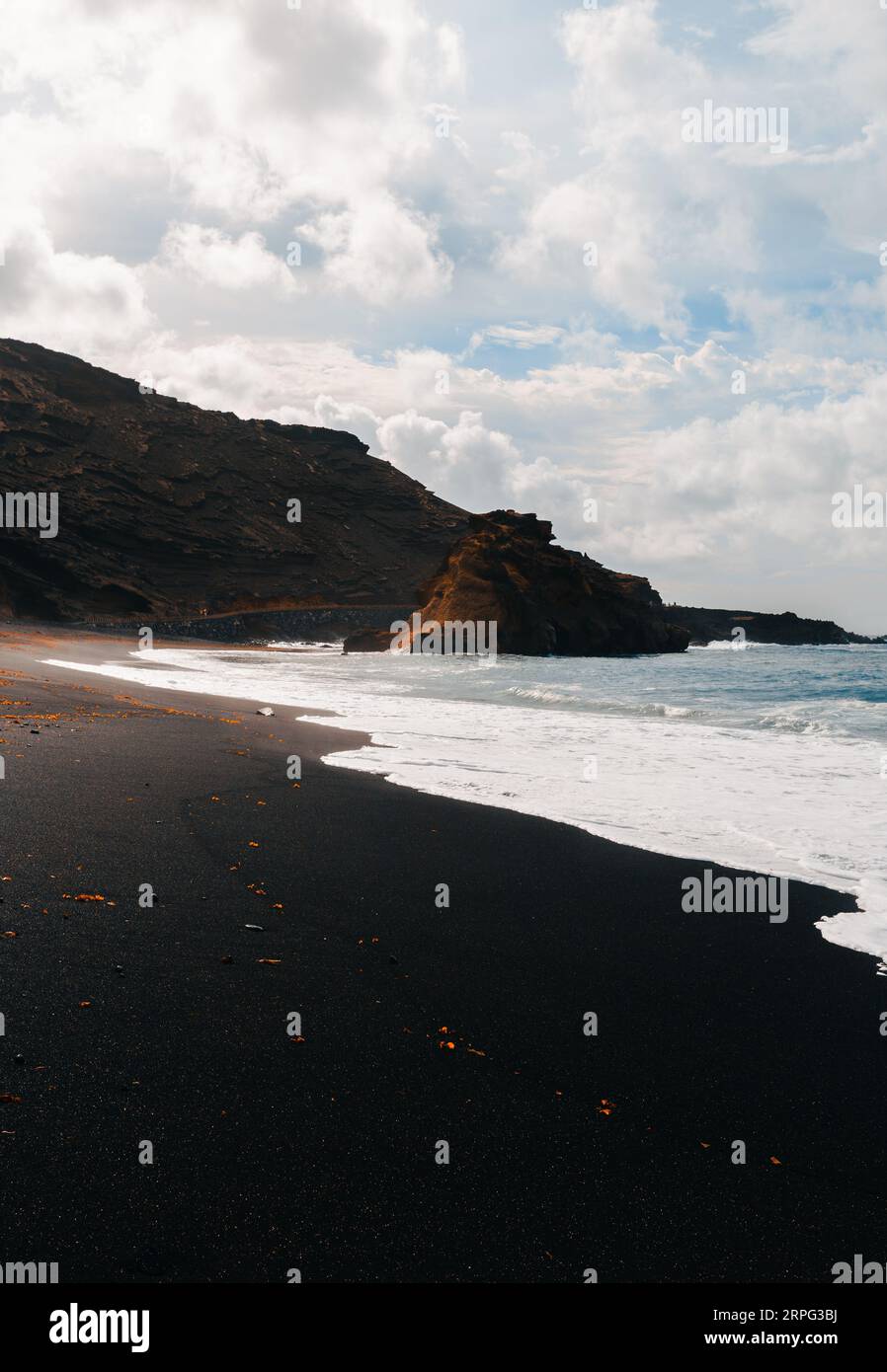 Vertical photo of black sand El Golfo beach in volcanic island Lanzarote (Canary Islands) with strong waves in blue ocean. Cliff in wild black sand be Stock Photo