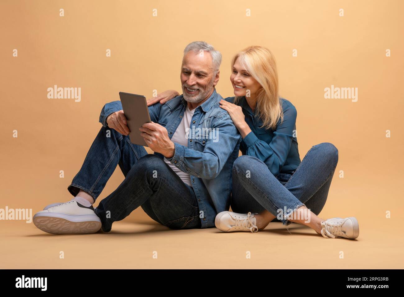 Positive senior couple using digital tablet, beige background Stock Photo