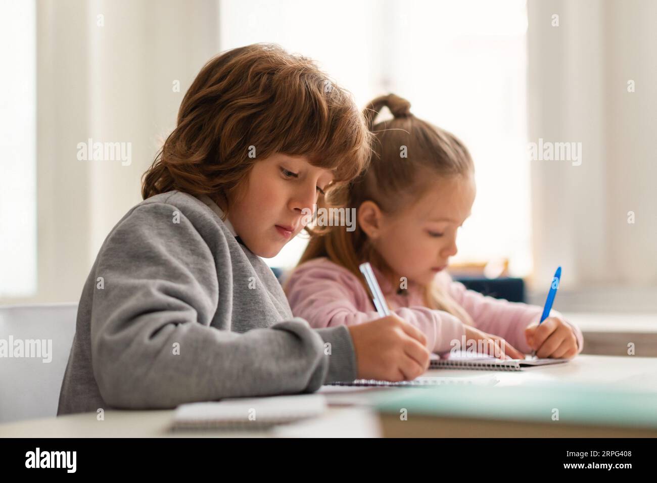 Schoolkids writing in workbooks during the lesson, sitting at desk in classroom at elementary school Stock Photo