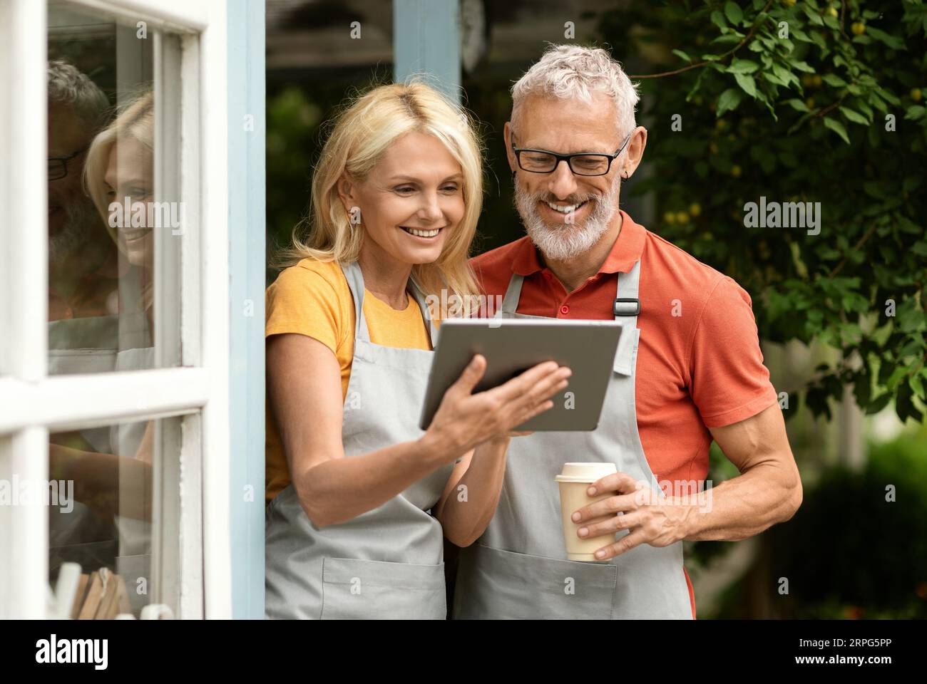 Happy mature couple drinking coffee and using digital tablet outdoors Stock Photo