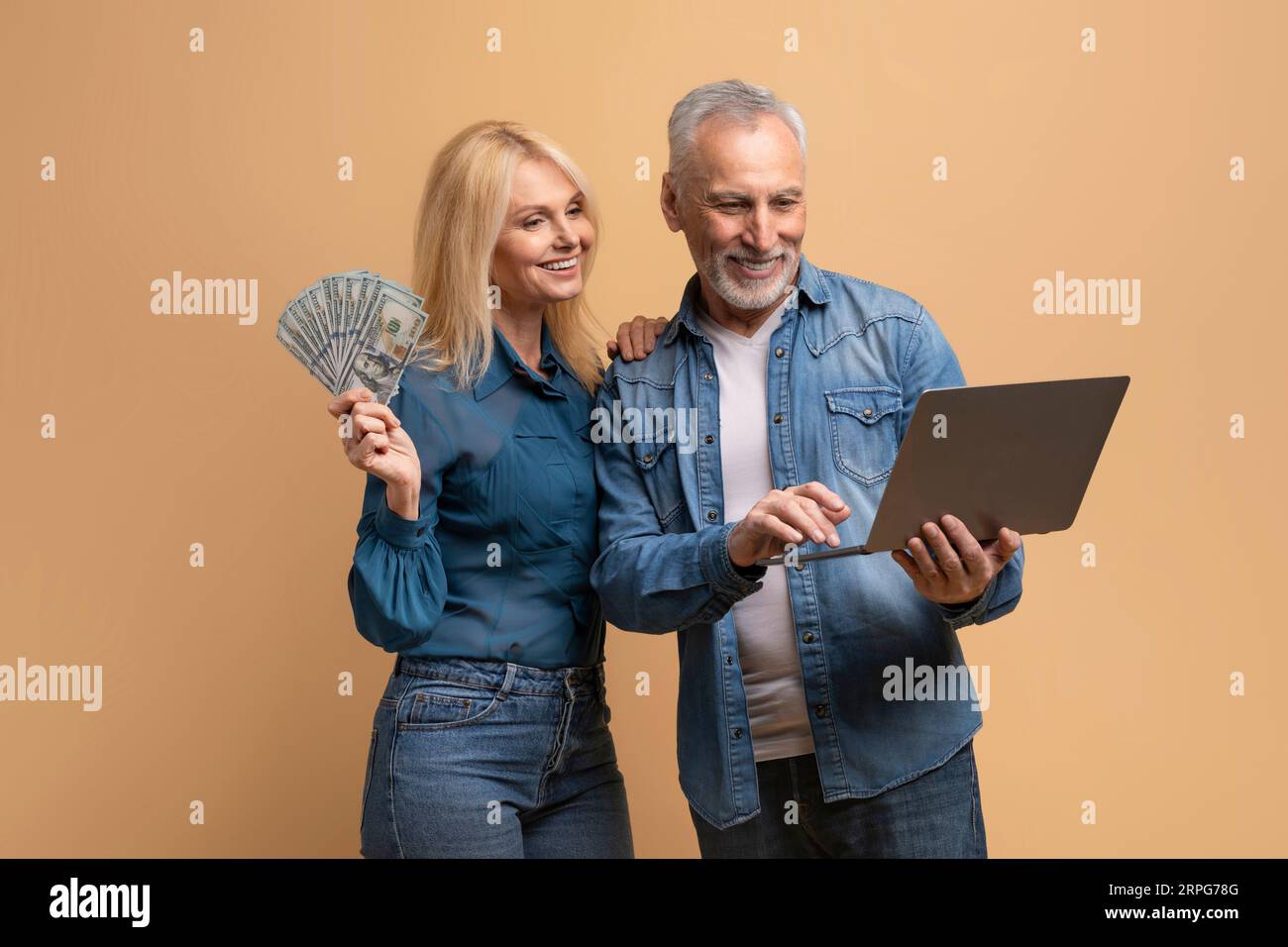 Happy elderly couple spouses using computer laptop, holding cash Stock Photo