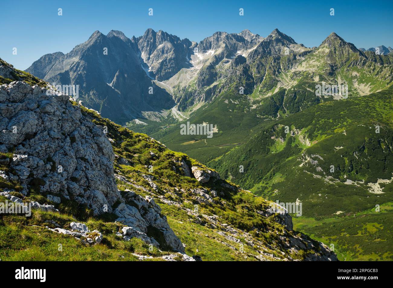 Mountain landscape, where the High Tatras meet the Belianske Tatras, bathed in sunlight and surrounded by emerald-green meadows Stock Photo