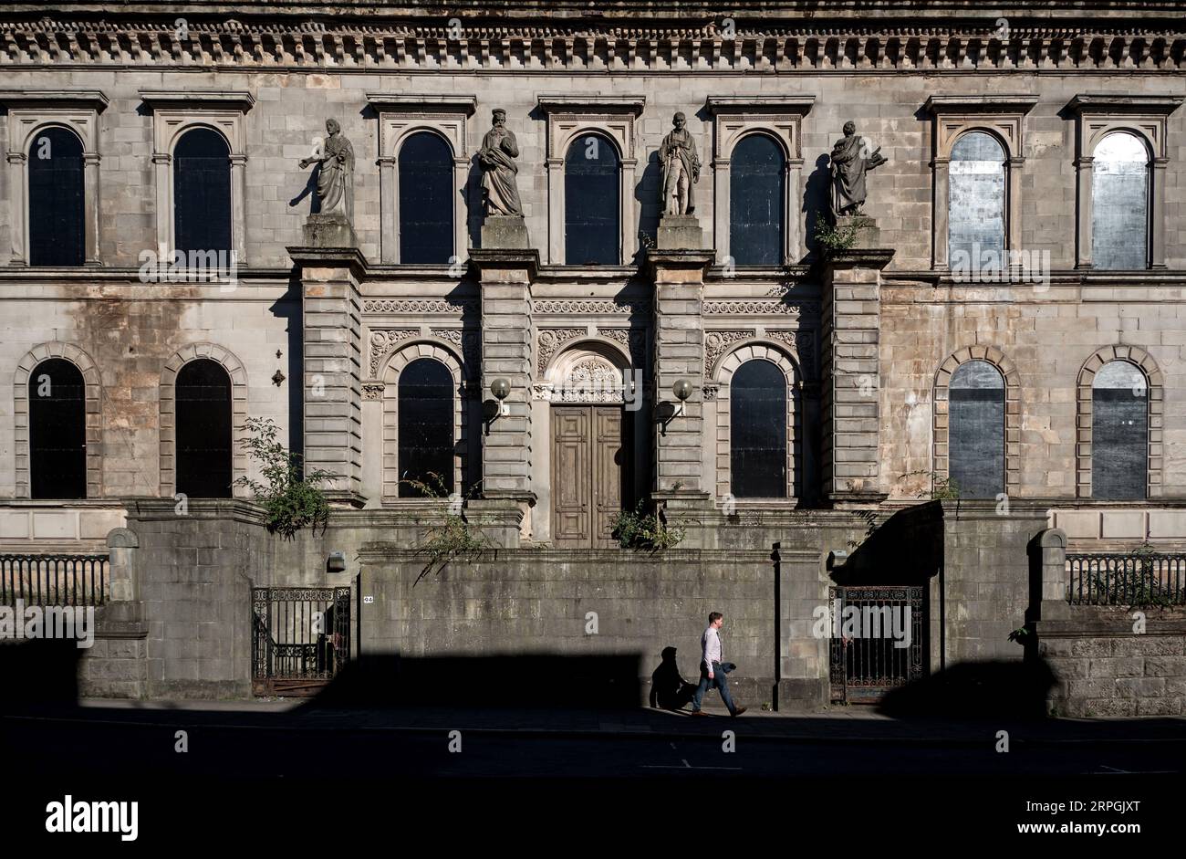 Man walking by the derelict old Glasgow Royal High School building featuring the statues of Cicero, Galileo, James Watt and Homer. Stock Photo
