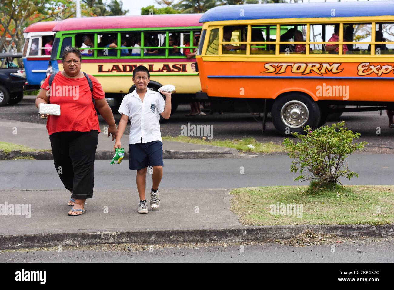 191023 -- APIA, Oct. 23, 2019 -- A woman and a boy get off from a public bus at the main bus station of Apia, capital of Samoa, Oct. 21, 2019. Most public buses in Samoa have been refitted from used trucks imported from overseas. Often featuring wild colours and creative body paintings, the buses make an attractive vista in this island country. For ventilation purposes, there are typically no window glasses in a bus passenger section and its rear end is openable. As the buses tend to go slowly on the island s bumpy mountainous roads, any sensible passenger would not choose to stand in the buse Stock Photo