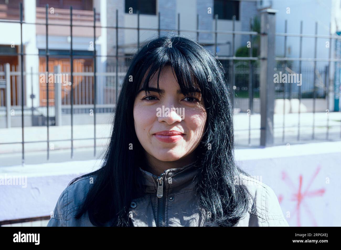 portrait of young venezuelan latina woman with black hair with bangs, wearing jacket for cold, standing outdoors at sunset looking at camera happily. Stock Photo