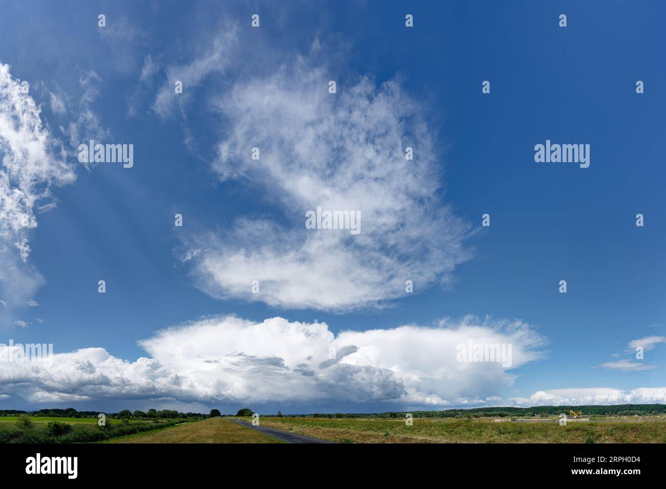 View along the dike at the German-Polish border river Oder to a big thunderstorm front and further cloud formations, wide flat landscape, a road as vi Stock Photo
