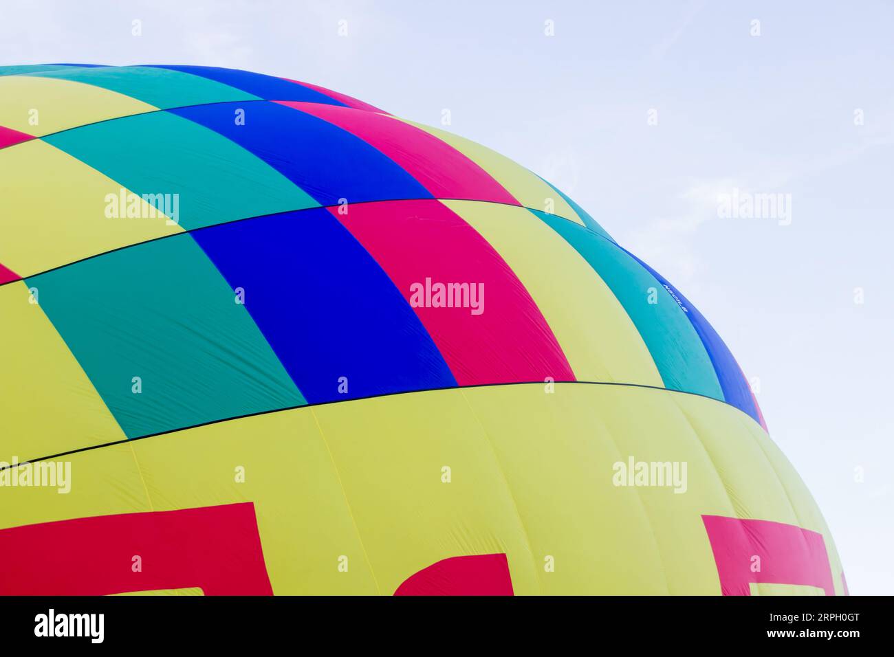 A hot air balloon is being inflated and it is only partially filled. The balloon is make up of squares of color that include blue, greened and yellow. Stock Photo