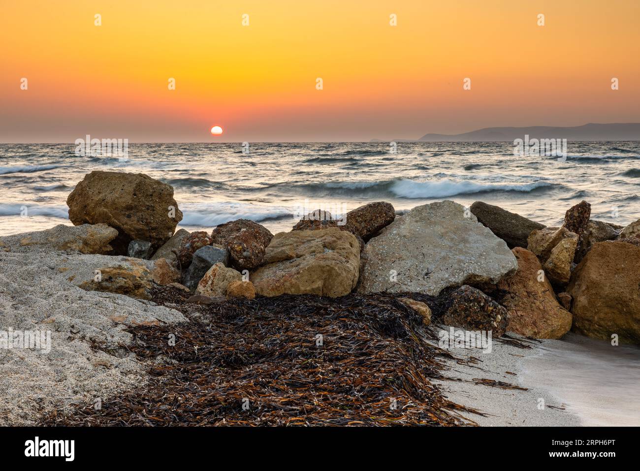 Embrace the ethereal beauty of the twilight hour on this tranquil beach adorned with scattered seaweed. The rocky breakwater stands as a sentinel agai Stock Photo