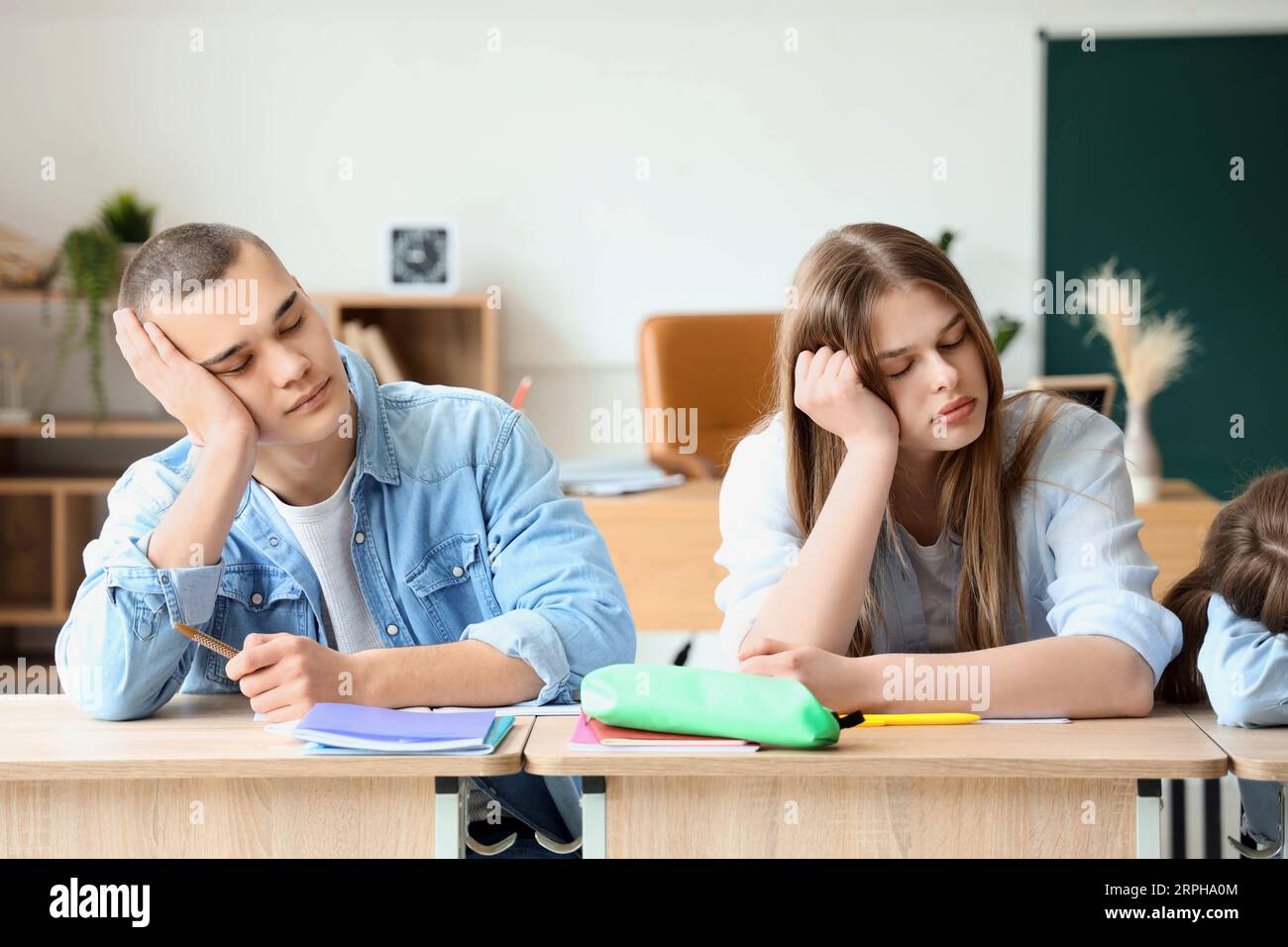 Tired sleepy classmates sitting at desks in classroom Stock Photo