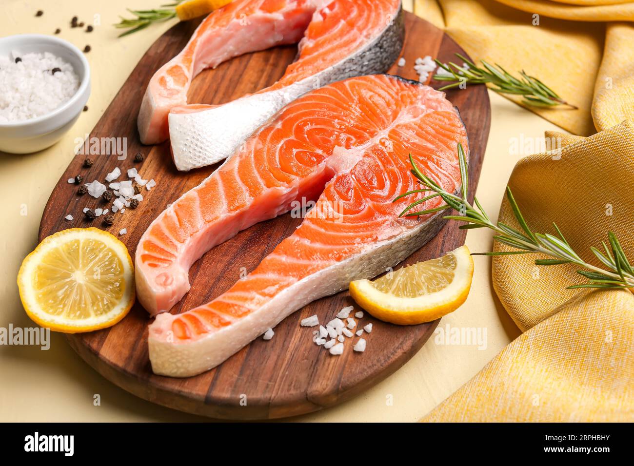 Wooden board with raw salmon steaks and different spices on yellow ...