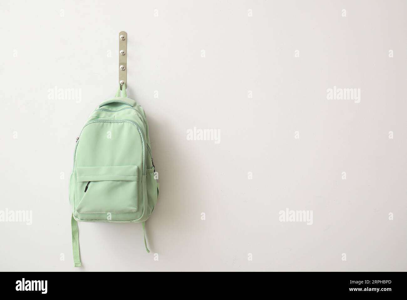 School backpack hanging on light wall Stock Photo