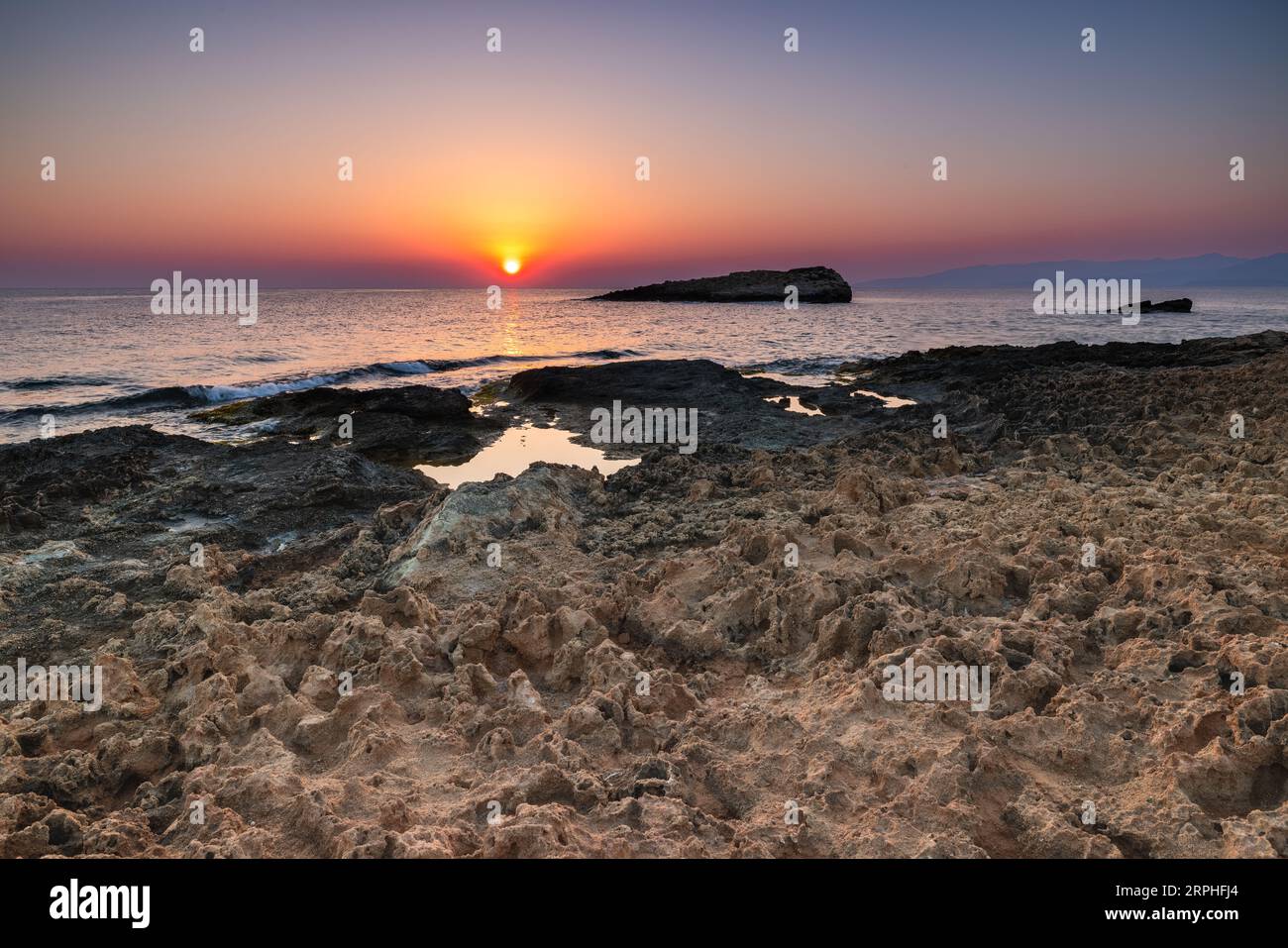 Experience the grace of nature as tranquil pools of water adorn the rugged coastal landscape in Crete. As the first light of day emerges on the horizo Stock Photo