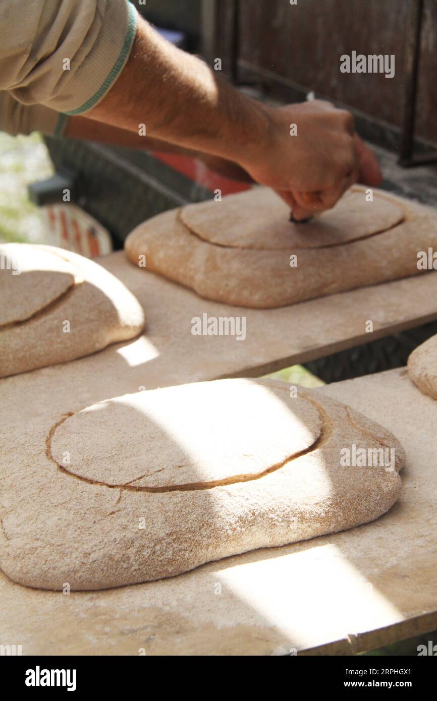 Baker cutting a pattern in the dough with a scoring tool Stock Photo