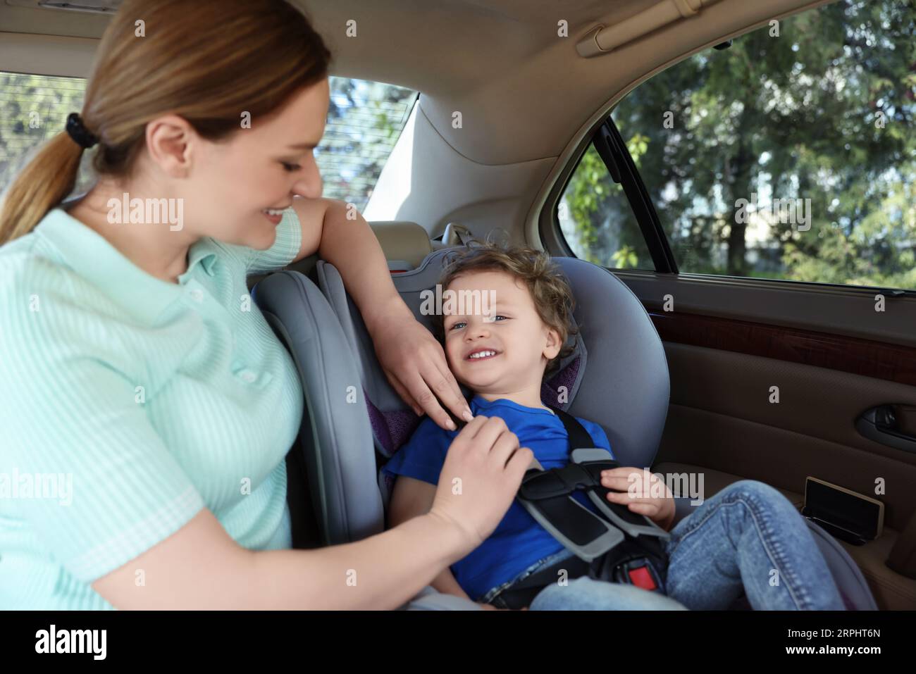 Mother fastening her son in child safety seat inside car Stock Photo ...