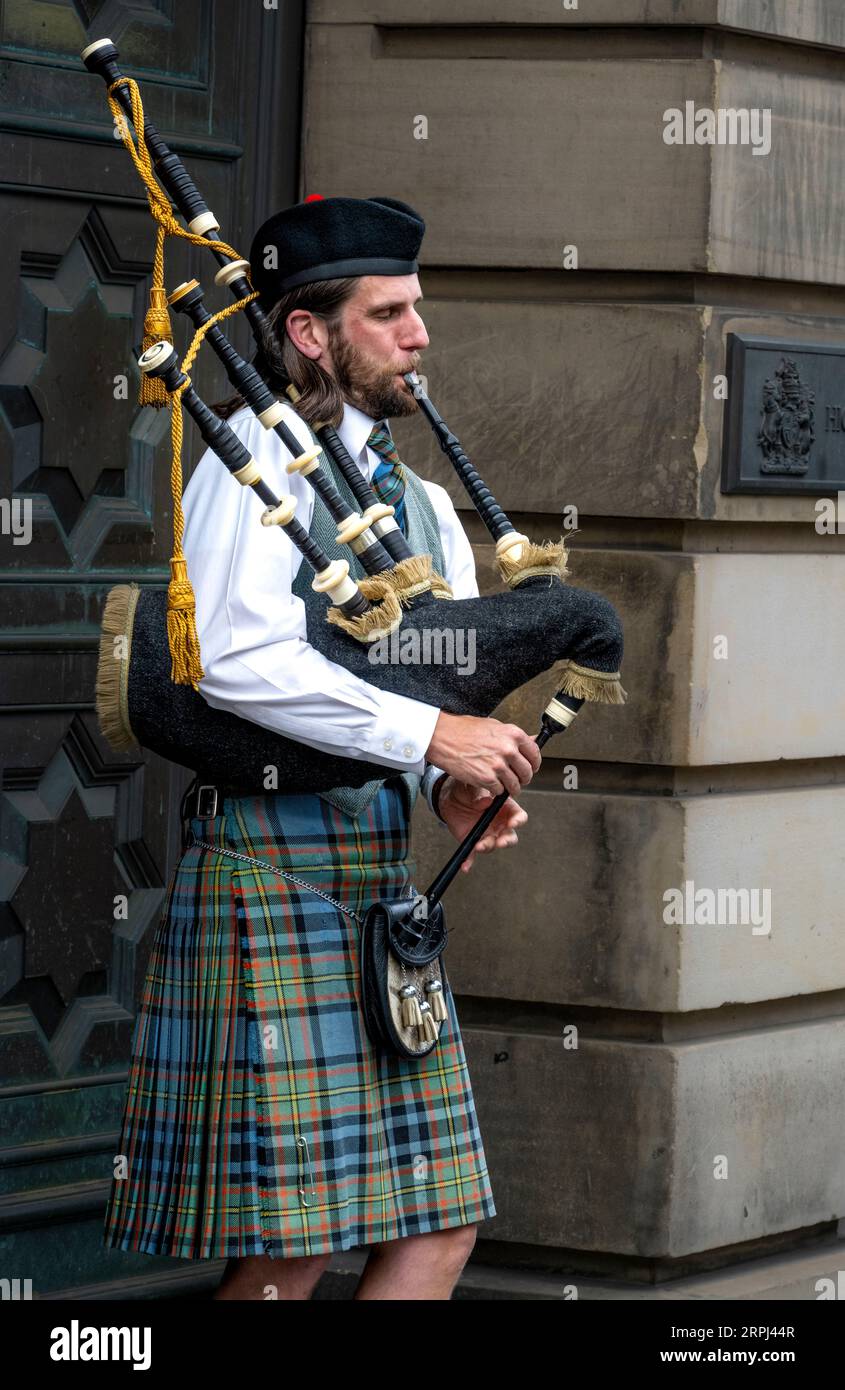 man playing the bagpipes dressed in traditional Scotish clothing on the Royal Mile in Edinburgh Scotland Stock Photo