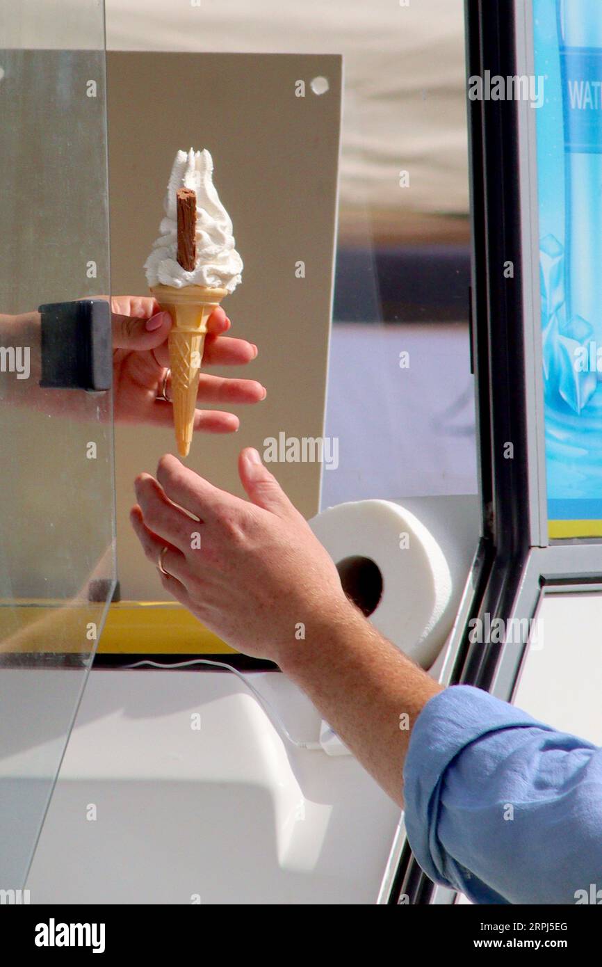 A freshly served 99 Flake is passed down to a happy customer by an ice cream vendor at the van’s serving window during a busy local food festival. Stock Photo