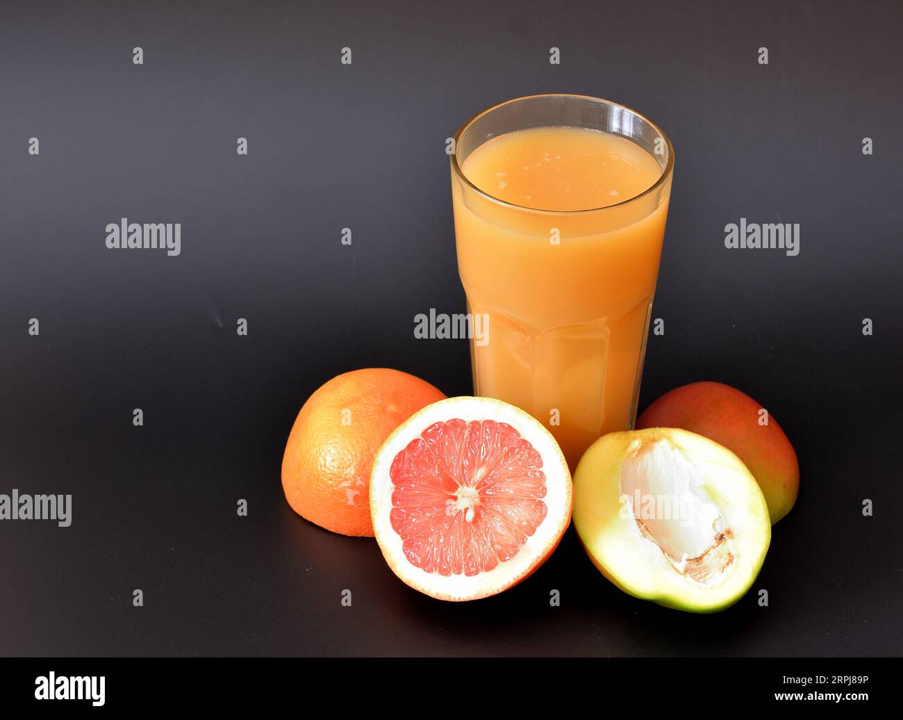 A glass of fruit juice on a black background, next to the halves of a ripe grapefruit and mango. Close-up. Stock Photo