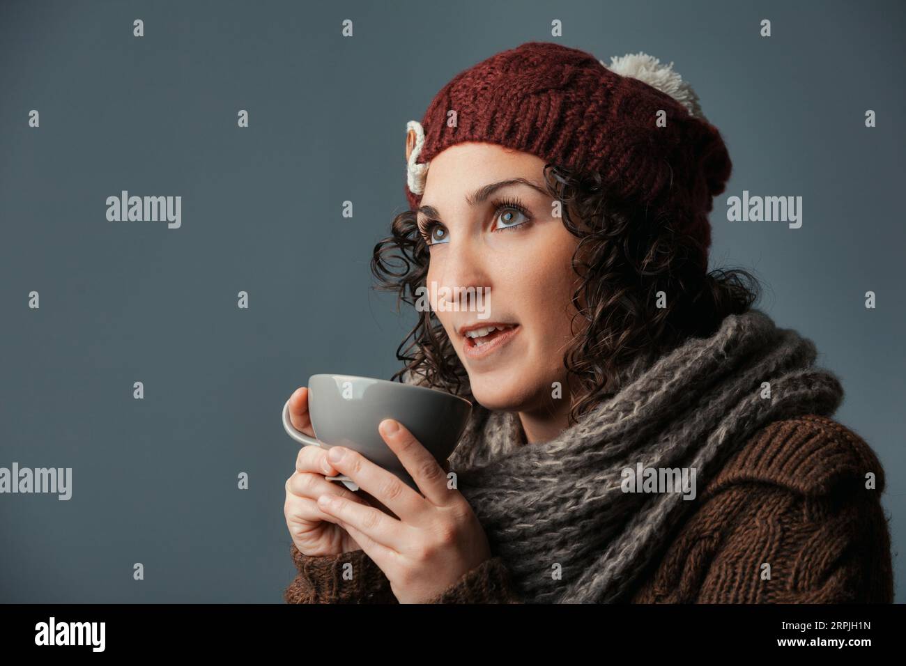 Embraced by winter, a woman in woolen attire sips a comforting drink
