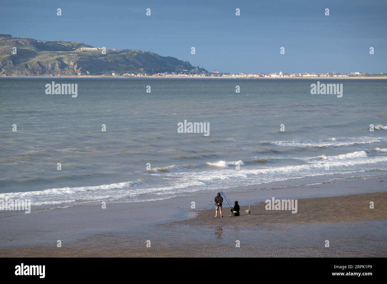 People fishing on the beach in North Wales, with Landudno and the Great Orme in the backgroup. Wales, UK. Stock Photo
