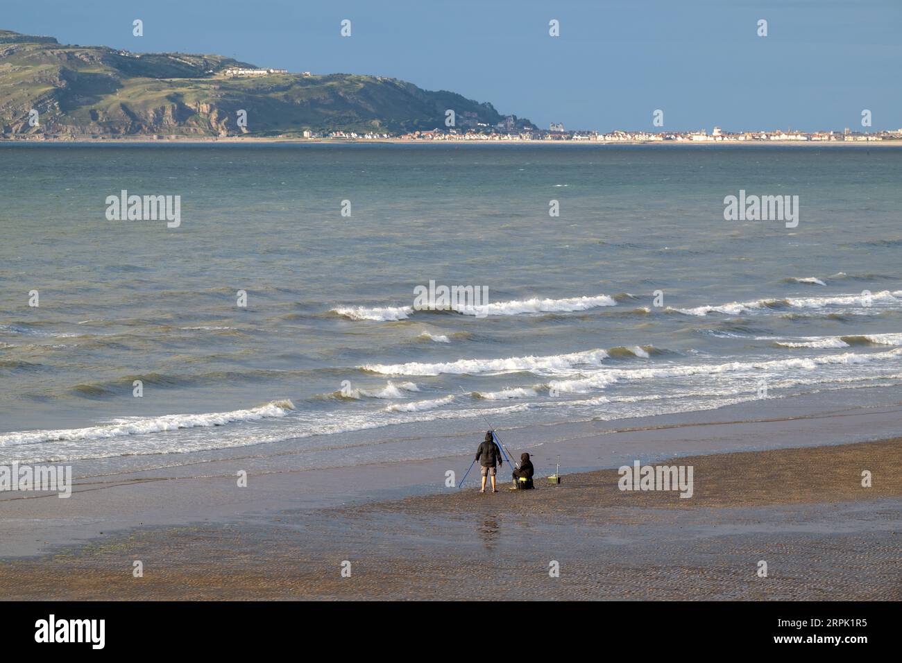People fishing on the beach in North Wales, with Landudno and the Great Orme in the backgroup. Wales, UK. Stock Photo