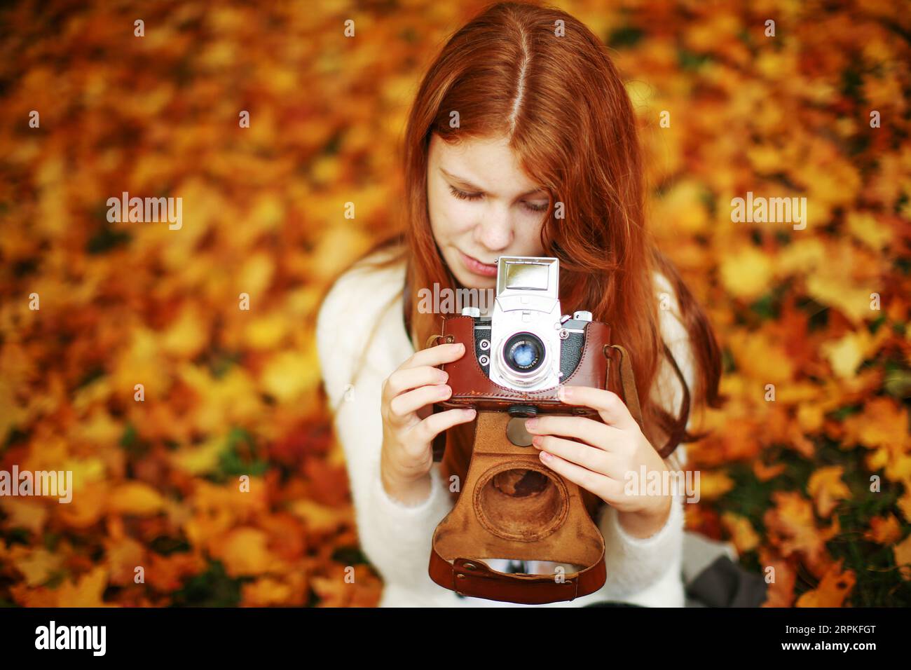 Little red-haired girl with a retro camera in the autumn park. Child photographer. Stock Photo