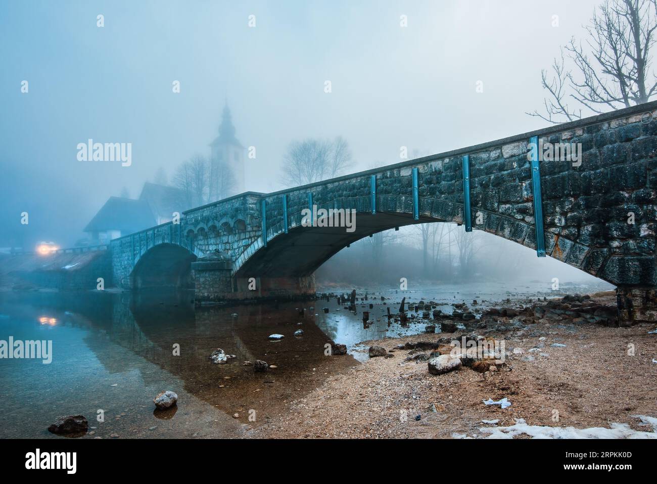 Old stone bridge at Bohinj lake in foggy morning, tranquil scene from Slovenia's travel destination in dawn, selective focus Stock Photo