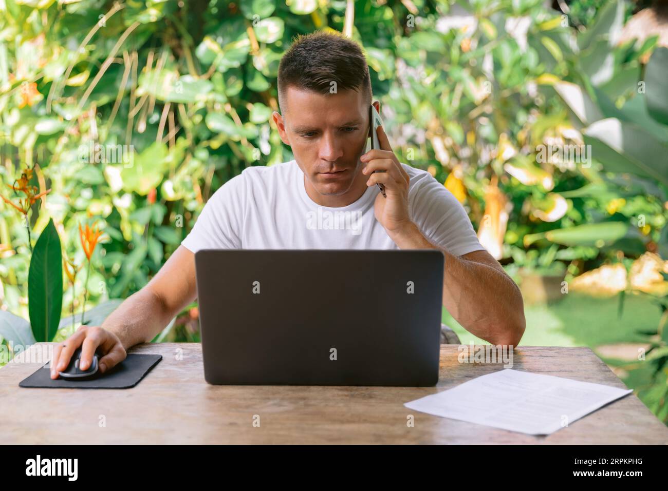 Software designer discussing a new project with his client on the phone. Serious man working on a laptop in an open plan office. Stock Photo