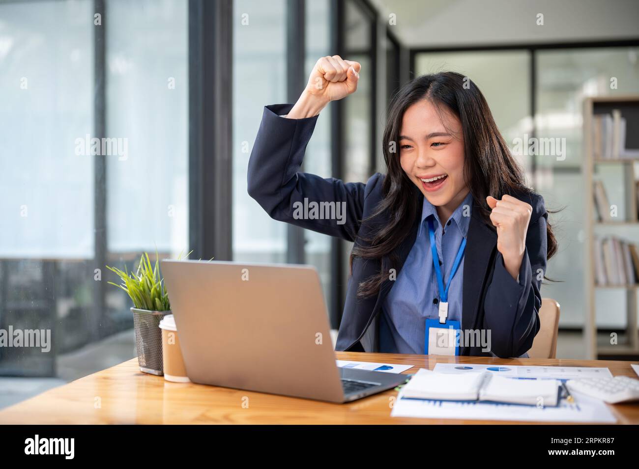 A cheerful young Asian businesswoman is looking at her laptop screen ...