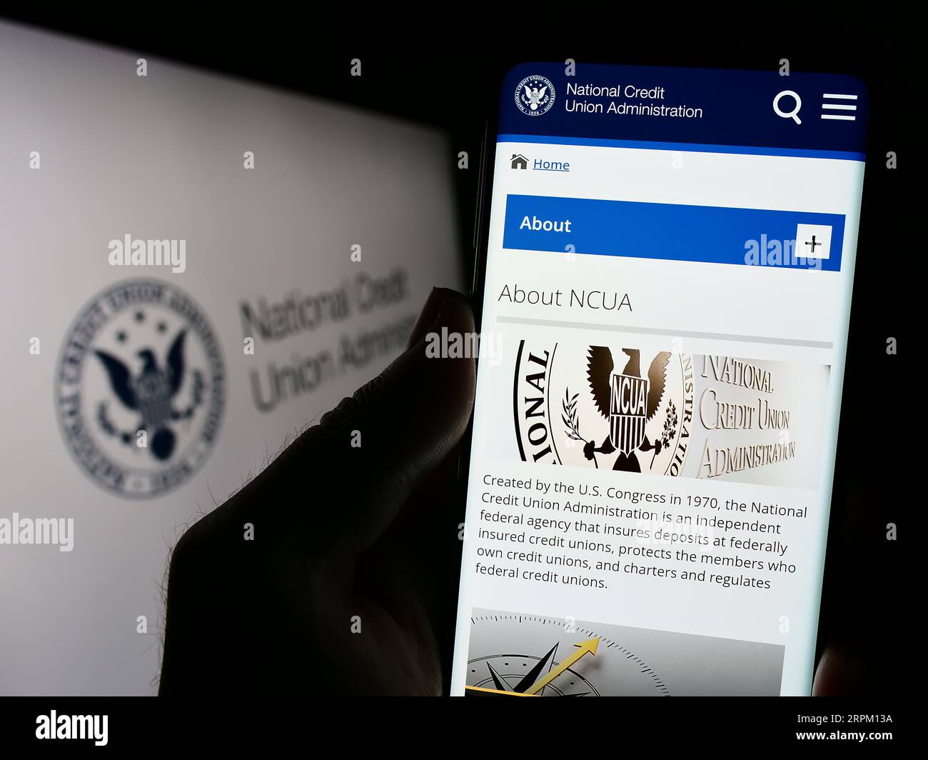 Person holding cellphone with website of National Credit Union Administration (NCUA) on screen in front of seal. Focus on center of phone display. Stock Photo