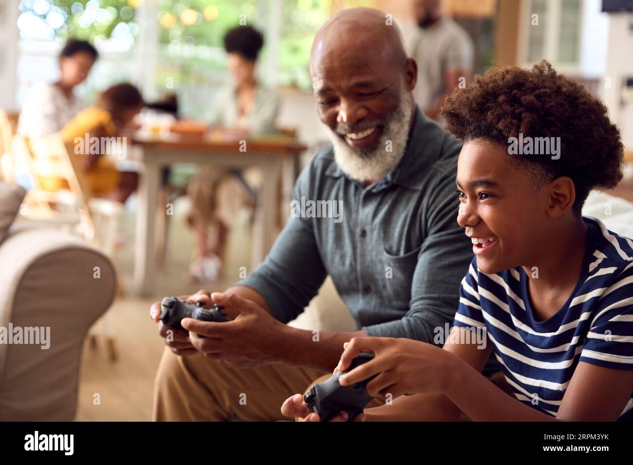 Grandfather And Grandson Sitting On Sofa At Home Playing Video Game Together Stock Photo