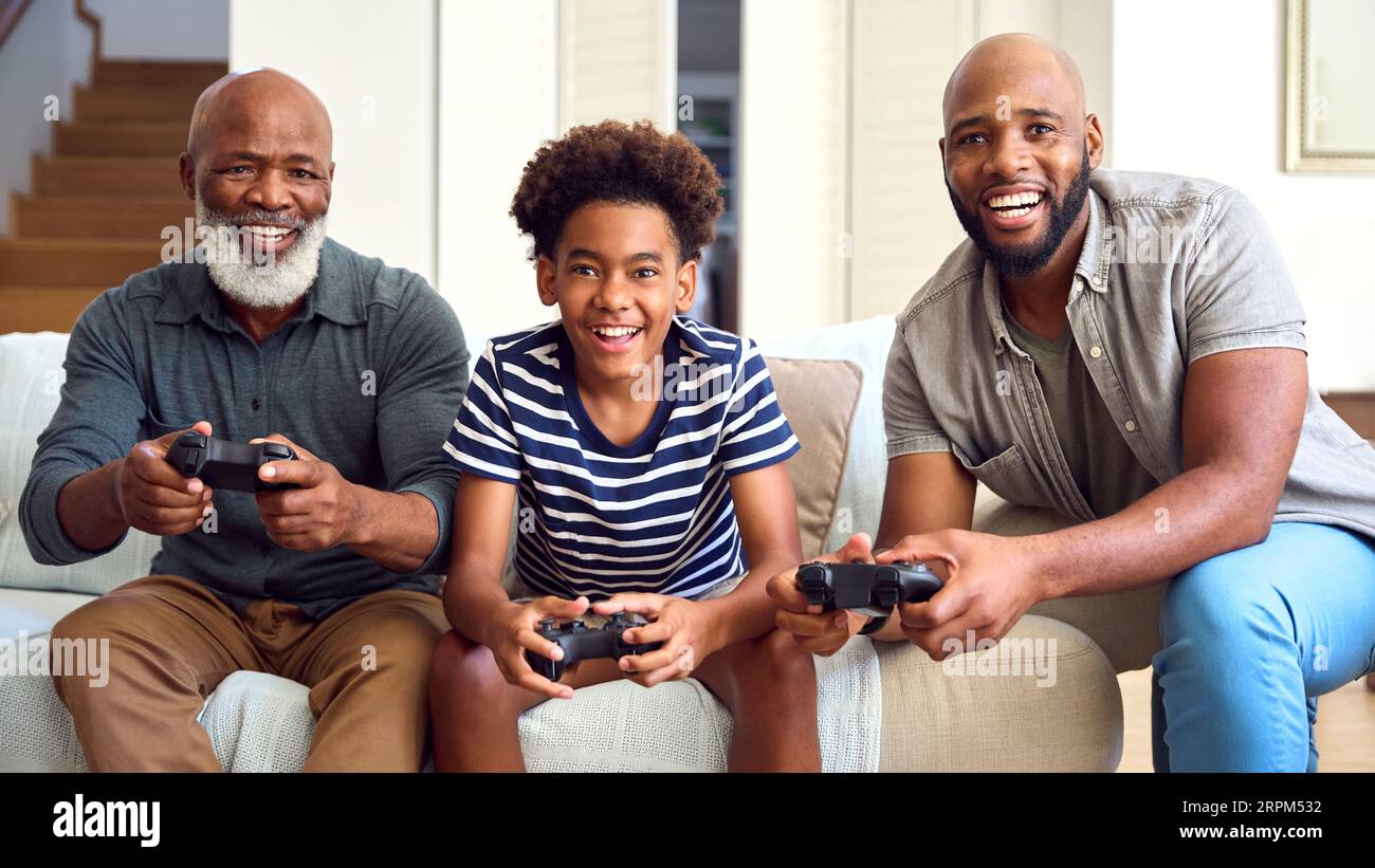 Multi-Generation Male Family Sitting On Sofa At Home Playing Video Game Together Stock Photo